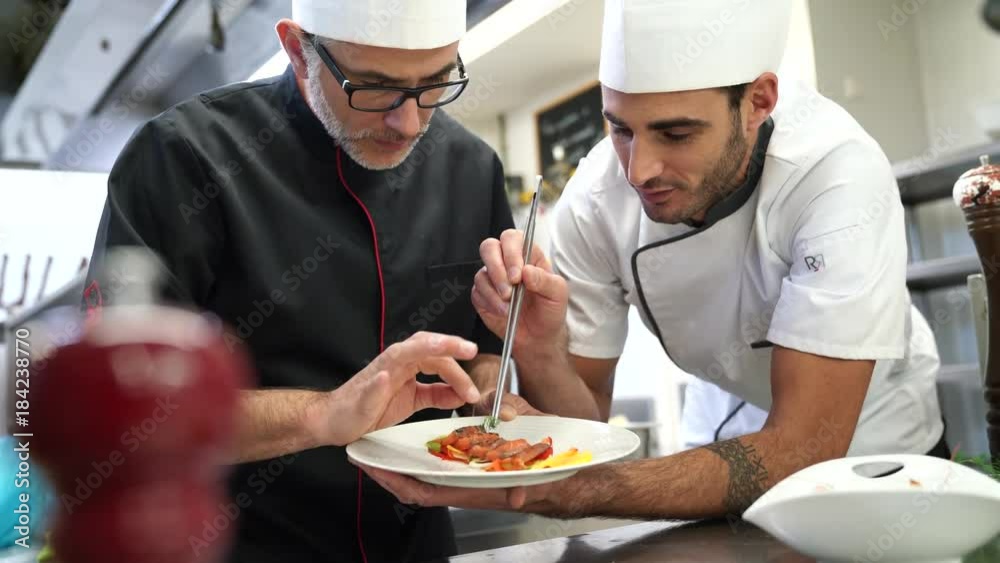 Cook chef teaching young cook to prepare dish