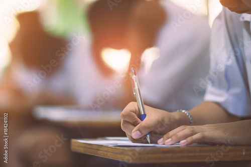 Closeup to hand of student holding pen and taking exam in classroom with stress for education test .