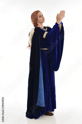  full length portrait of girl wearing long blue velvet gown and fur lined cloak, standing pose on white background.