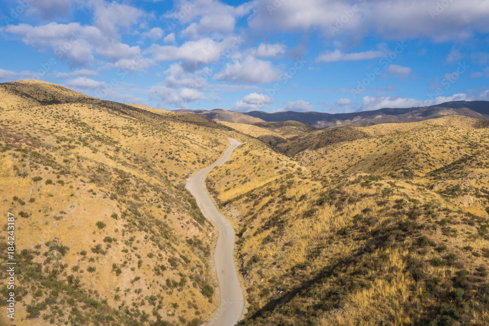 Drone photograph of asphalt road leading through the dry hills of southern California canyons.