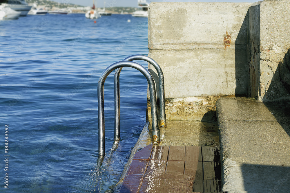 chromed iron railing for the descent to the sea on the background of blue sea and yachts