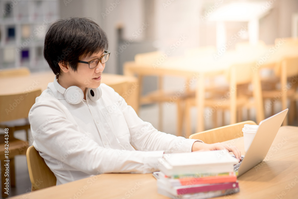 Young Asian university student working with laptop computer and book in library for education research, self learning and college lifestyle concepts Young Asian university student working with laptop computer and book in library for education research, self learning and college lifestyle concepts