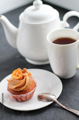 A teapot, a cup of tea and a caramel cupcake.