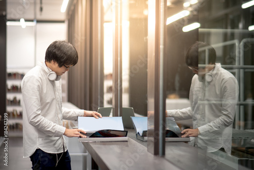 Young Asian man dressed in casual style opening book in library. Male university student research information for self-learning.