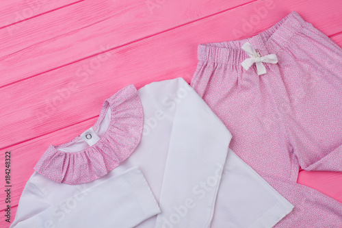 Pink and white pajama set for little girl. Cute top and pants. Clothes on wooden background. © DenisProduction.com