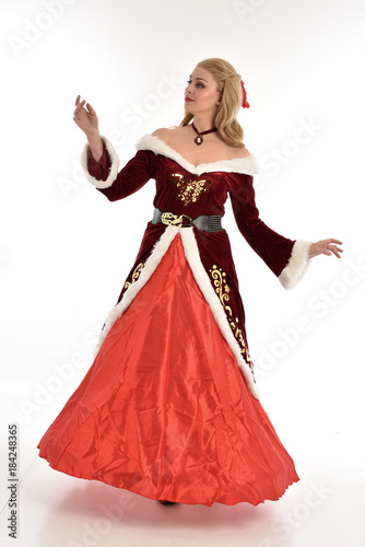 full length portrait of pretty blonde lady wearing red and white christmas inspired costume gown, standing pose on white background.