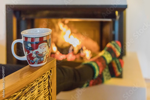Christmas mug in the foreground, fireplace with logs in the background. Winter and Christmas holidays concept.