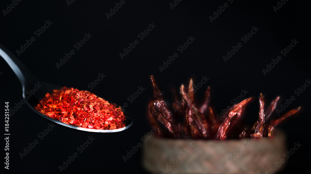 dried chili pepper powder in a spoon with dried chili pepper in a basket as background