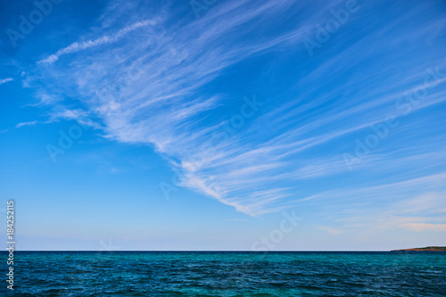Simple blue sky with diagonal stripes of clouds over the sea