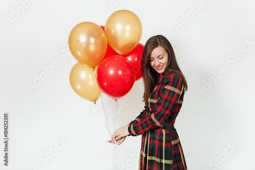 Beautiful caucasian young happy woman in long plaid checkered dress with shy charming smile, red, yellow golden balloons, celebrating birthday, on white background isolated. Holiday, party concept.