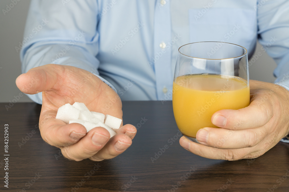 Man sits at the table and has a glass of orange juice in front of him in his hand he holds many pieces of sugar cubes Man sits at the table and has a glass of orange juice in front of him in his hand he holds many pieces of sugar cubes