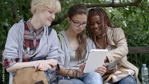 Three teen girls smiling and making faces at camera while taking selfie with digital tablet in park photo