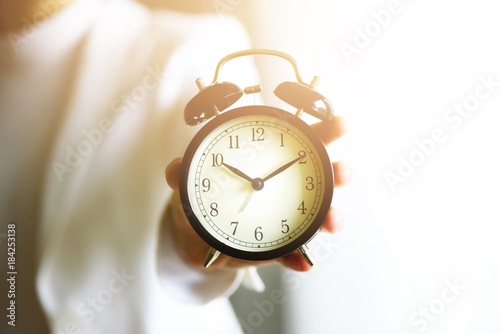 Classic black alarm clock in a hand. Sunny morning light. Copy space.