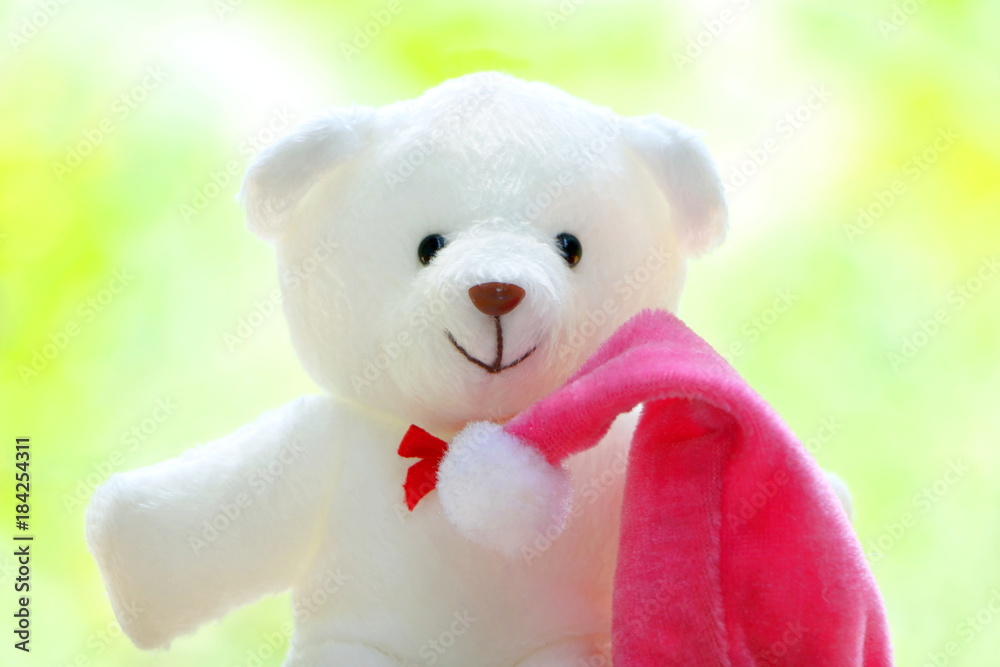 Closeup one white teddy bear wear red bow with pink Christmas cap on green,yellow and white bokeh Closeup one white teddy bear wear red bow with pink Christmas cap on green,yellow and white bokeh