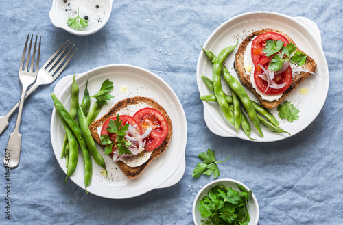 Grilled sandwich with cream cheese, tomatoes and boiled green beans - a healthy breakfast or snack on a blue background, top view