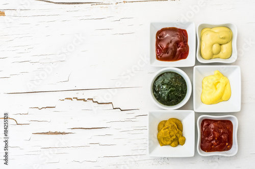 Classic set of sauces in square white sausers on surface with cracked paint. Top view. photo