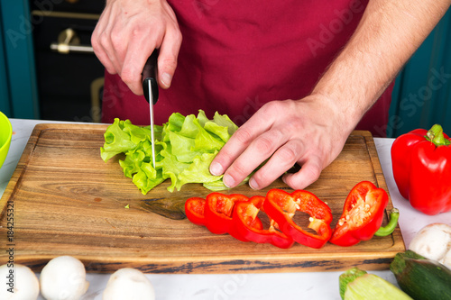 Hands cut green salad, red pepper, vegetables with knife
