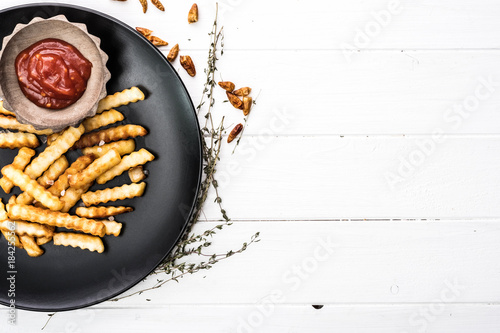 French potatoes on black plate with bowl of ketchup and sea salt. White wooden background.
