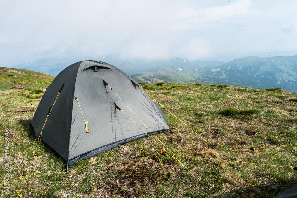 Grey tourist tent in camp among meadow in the mountain. Camping outdoor, grey tent in mountains