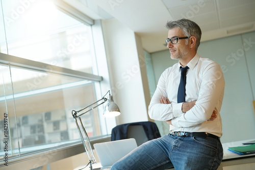 Confident businessman sitting on desk with arms crossed