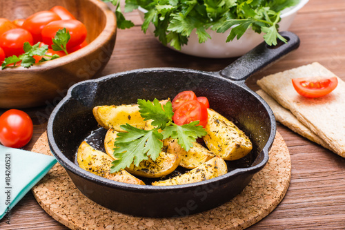 Sliced baked potatoes in an iron frying pan, cherry tomatoes and parsley leaves