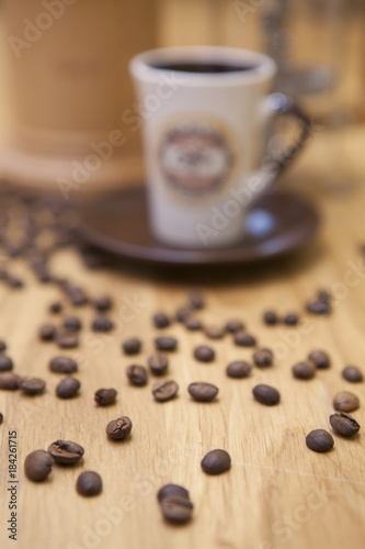 Spilled coffee beans. A cup of coffee and a background coffee maker. Shallow focus on coffee beans.
