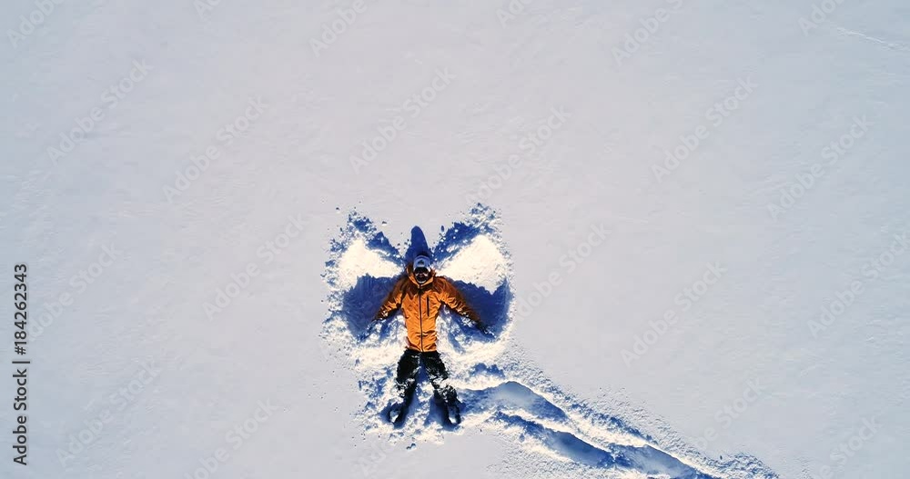 Vue rapprochée d'un homme qui souri en réalisant un ange allongé dans la neige - orange manteau montagne sourire bouge réflection hiver