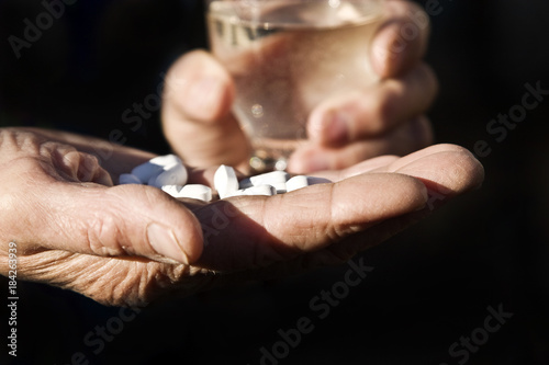 Hands of an old grandmother with pills on a black background closeup