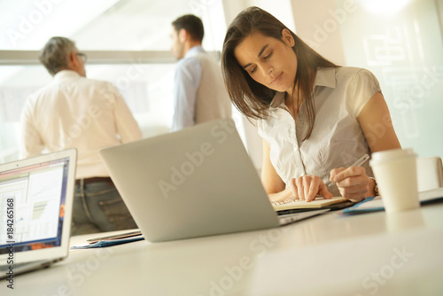 Businesswoman in office working on laptop computer  team in background