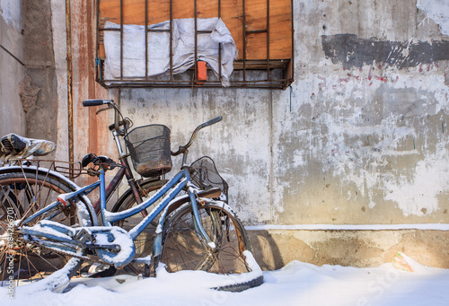 Snow covered old bicycles against a textured wall, Changchun, China