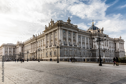 Facade of the Royal Palace of Madrid with tourists passing by its side
