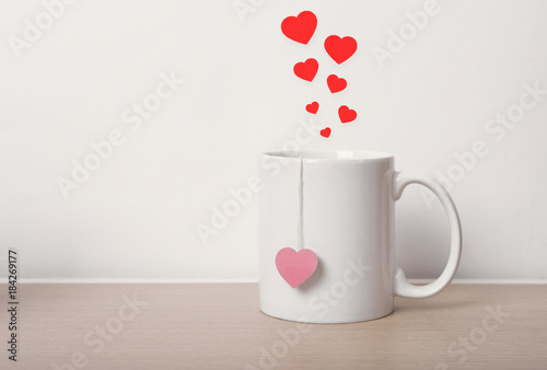 white tea cup with red heart on wooden table. vintage background.