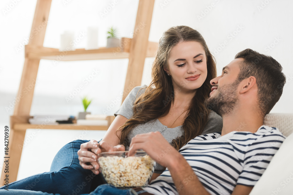 young couple eating popcorn on couch at home