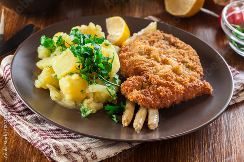 Homemade breaded viennese schnitzel with potato salad and asparagus on a plate