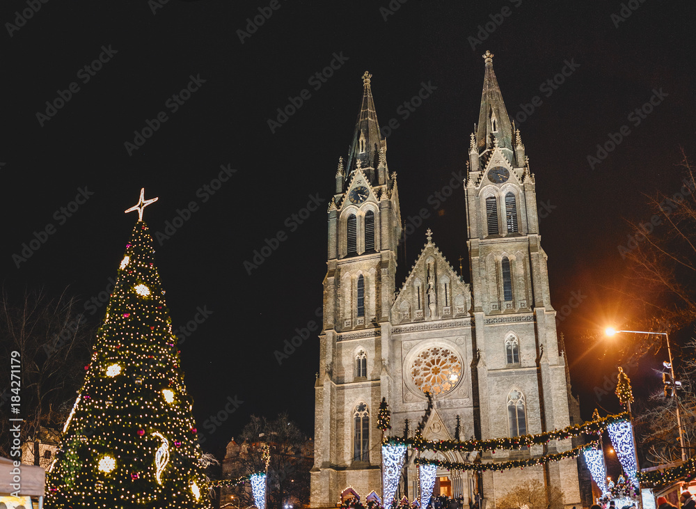 a souvenir fair and a beautifully decorated Christmas tree in Namesti Miru Square against the backdrop of the majestic building of the St. Ludmila Church