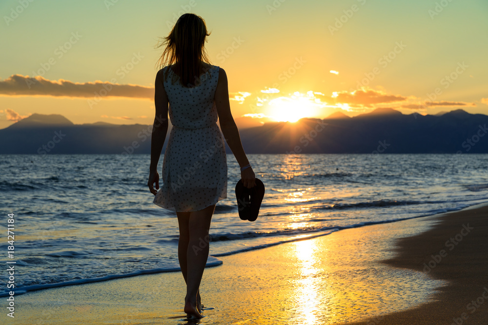 Junge, sexy Frau läuft flaniert am Strand Meer entlang. In der Hand hält  sie Flip Flops. Träumend Selfie mit Handy, Welliges Meer und oranger  Sonnenuntergang in den Bergen Stock Photo | Adobe