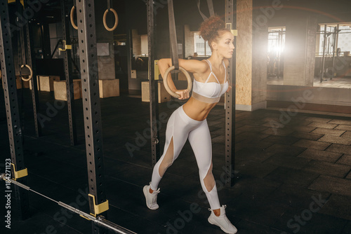 Muscle-up exercise athletic woman doing intense workout at the gym on gymnastic rings. Fit young woman holding gymnast rings at the gym looking away. Young caucasian woman exercising at gym. photo