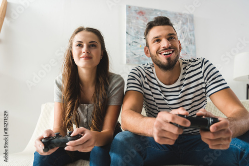 happy young couple playing games with gamepads at home