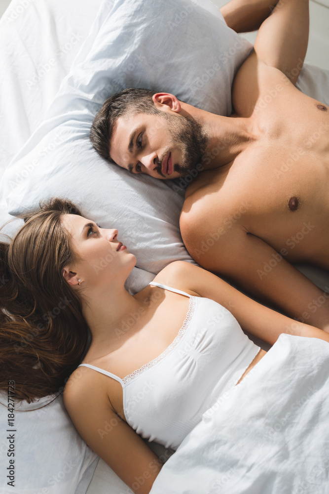 top view of young couple lying in bed and looking at each other in morning top view of young couple lying in bed and looking at each other in morning