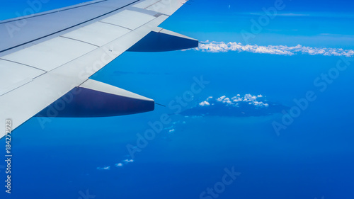 Wing of airplane with blue sky, cloud, island and sea.