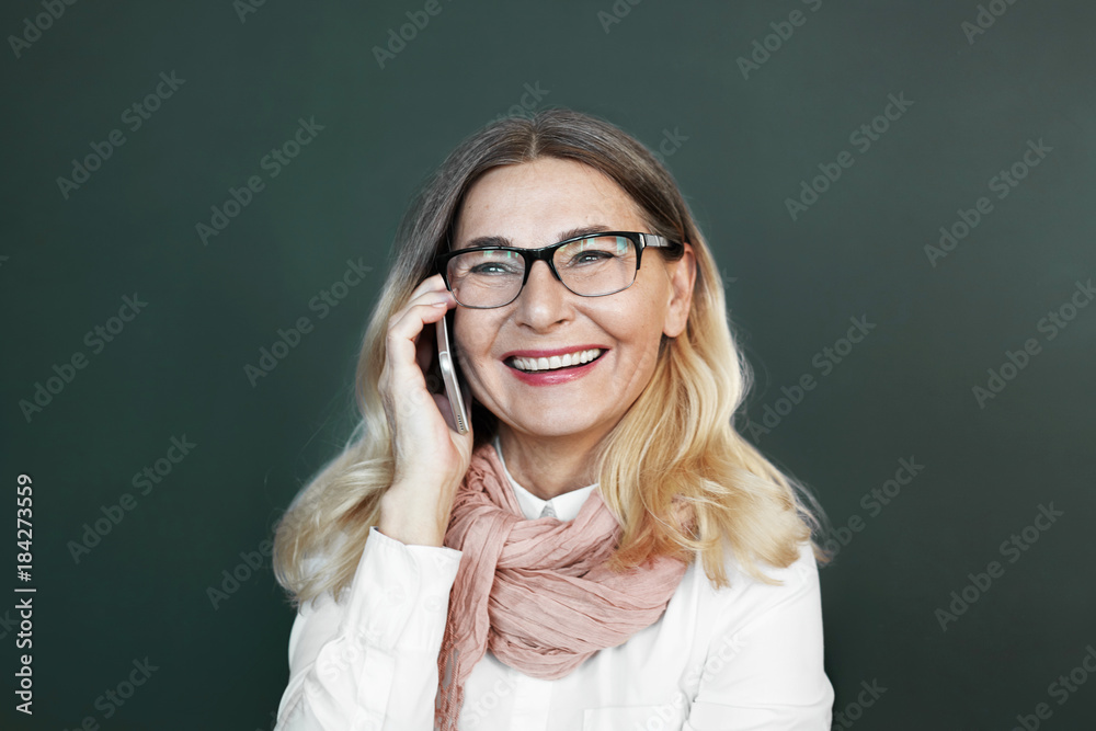 Senior people, modern technologies and electronic devices concept. Charismatic middle aged European woman in glasses grinning broadly while laughing at joke, speaking on phone to her friend Senior people, modern technologies and electronic devices concept. Charismatic middle aged European woman in glasses grinning broadly while laughing at joke, speaking on phone to her friend