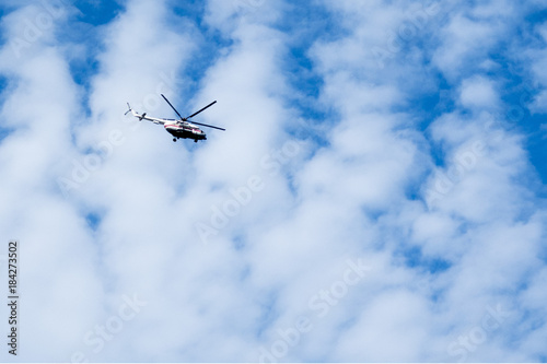 helicopter flies high in the sky against a background of clouds