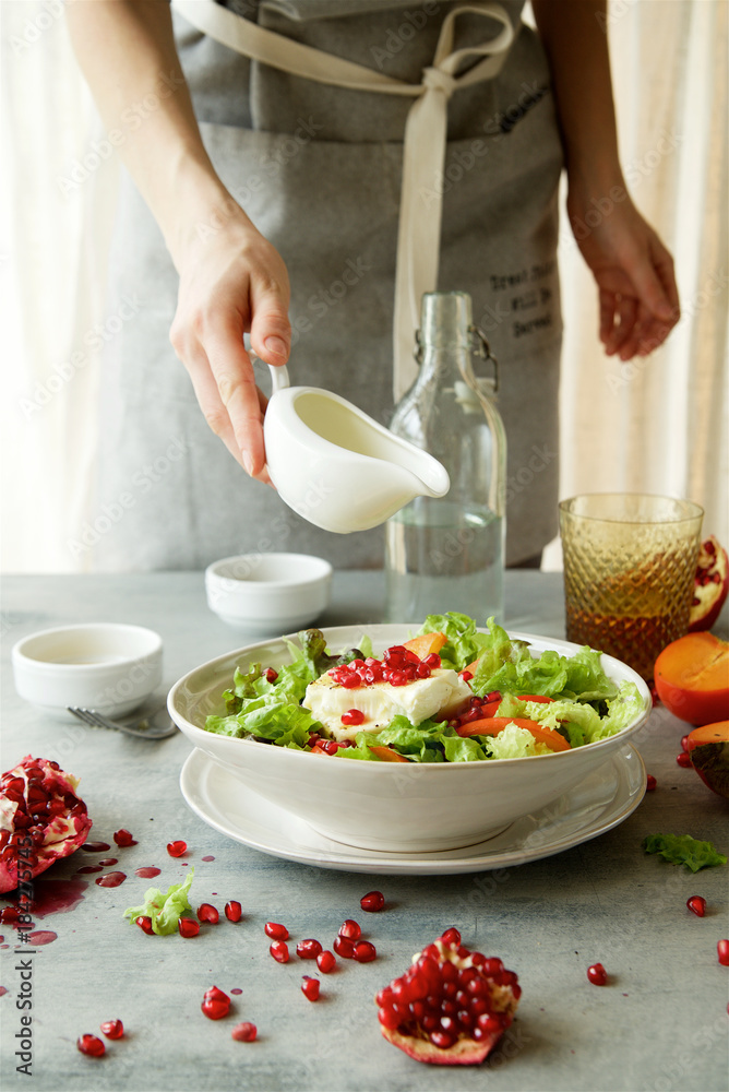 Cooking of seasonal salad with persimmon, pomegranate and dressing from honey and mustard 
