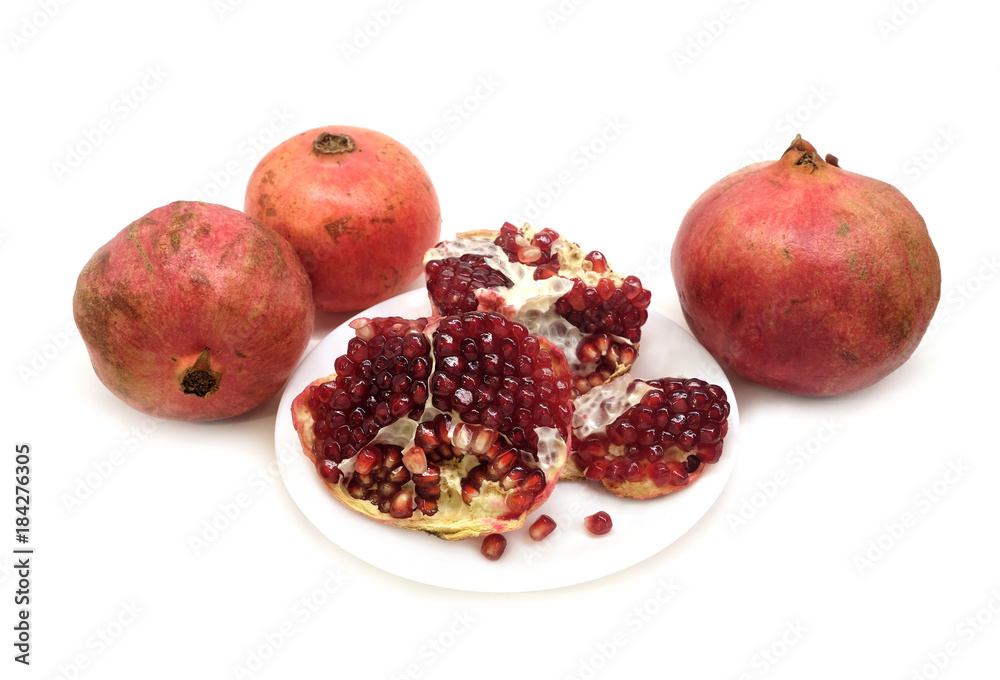 Whole and half pomegranates with ripe seeds on plate isolated on white background front view closeup Whole and half pomegranates with ripe seeds on plate isolated on white background front view closeup
