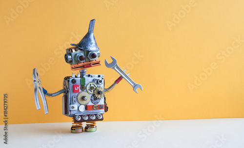 Friendly robot serviceman pliers handwrench. Fixing maintenance concept. Creative design toy with metal funnel hopper, cogs wheels gears silver metallic body. Yellow wall, beige floor background. Copy