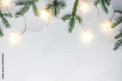 Christmas soft and cozy composition. Fir branches, handmade stars and light bulbs on a white background. Copy space. Top view