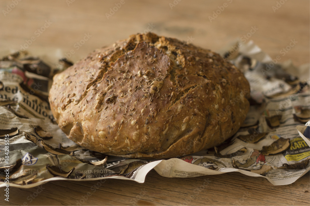 European cereal homemade loaf of bread on old newspapers with dried mushrooms European cereal homemade loaf of bread on old newspapers with dried mushrooms