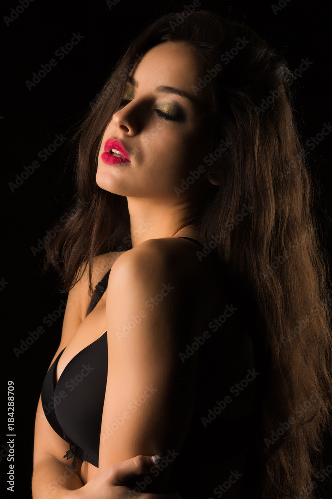 Luxury tanned woman with bright makeup and long hair posing in black bra. Shadow and light Luxury tanned woman with bright makeup and long hair posing in black bra. Shadow and light