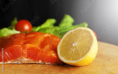 piece of red fish with lemon and cherry tomatoes on a wooden board on a black background