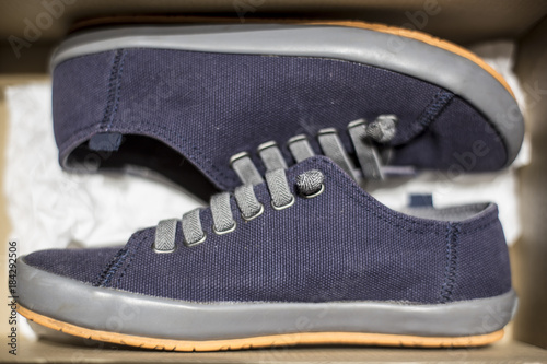 Stylish blue sneakers are stored inside a cardboard box. Close-up.